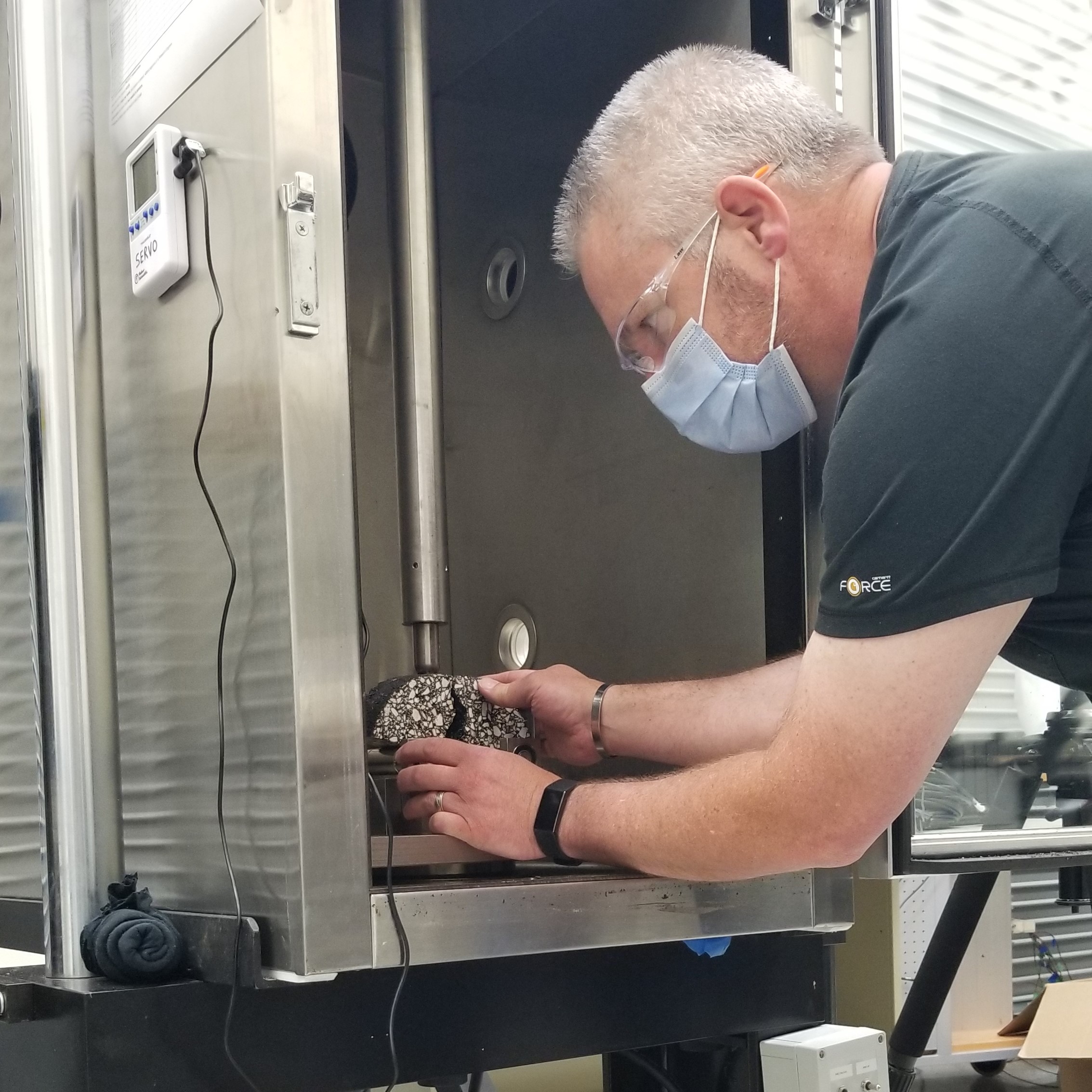 Greg Renshaw, ICT's senior research engineer, dons a facemask while removing a hot-mix asphalt sample after testing it in one of the center's servo-hydraulic test frames at ICT on July 7.