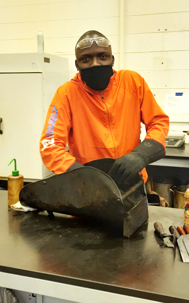 Abdulgafar Sulaiman, CEE doctoral student, cleans the chute after using it to mix and compact an asphalt specimen at ATREL in Rantoul, Ill. earlier in June.